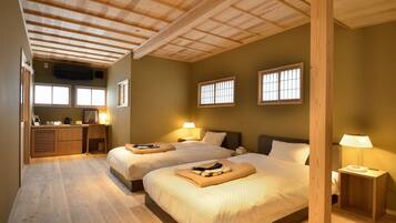 A hotel room with two beds, wooden flooring, a desk, and a kitchenette.