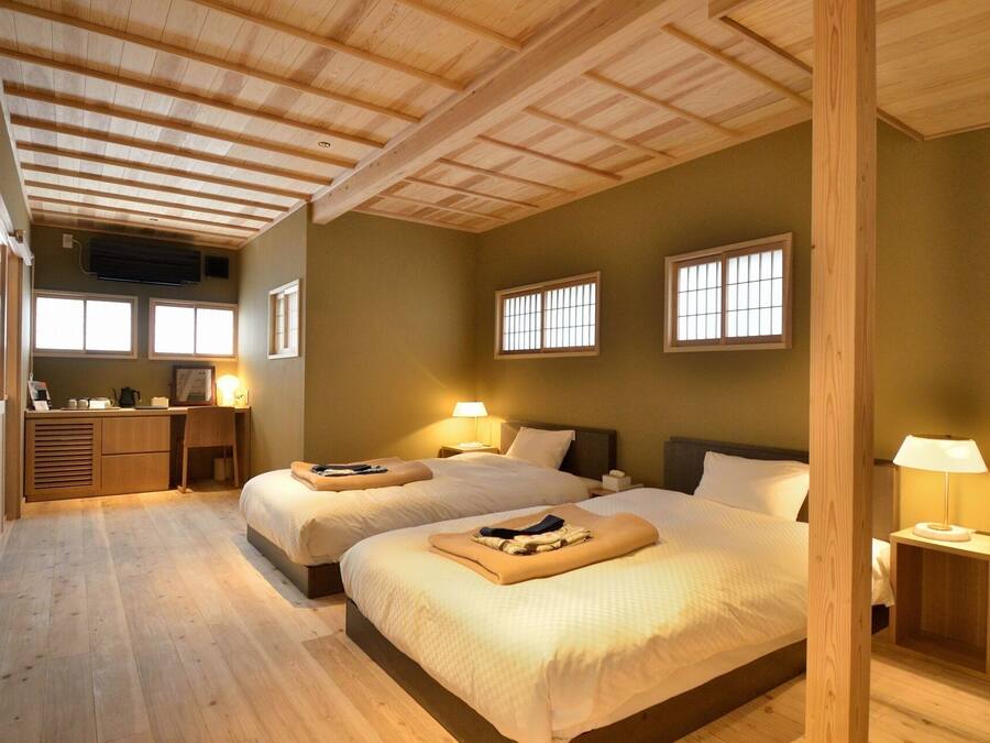 A hotel room with two beds, wooden flooring, a desk, and a kitchenette.