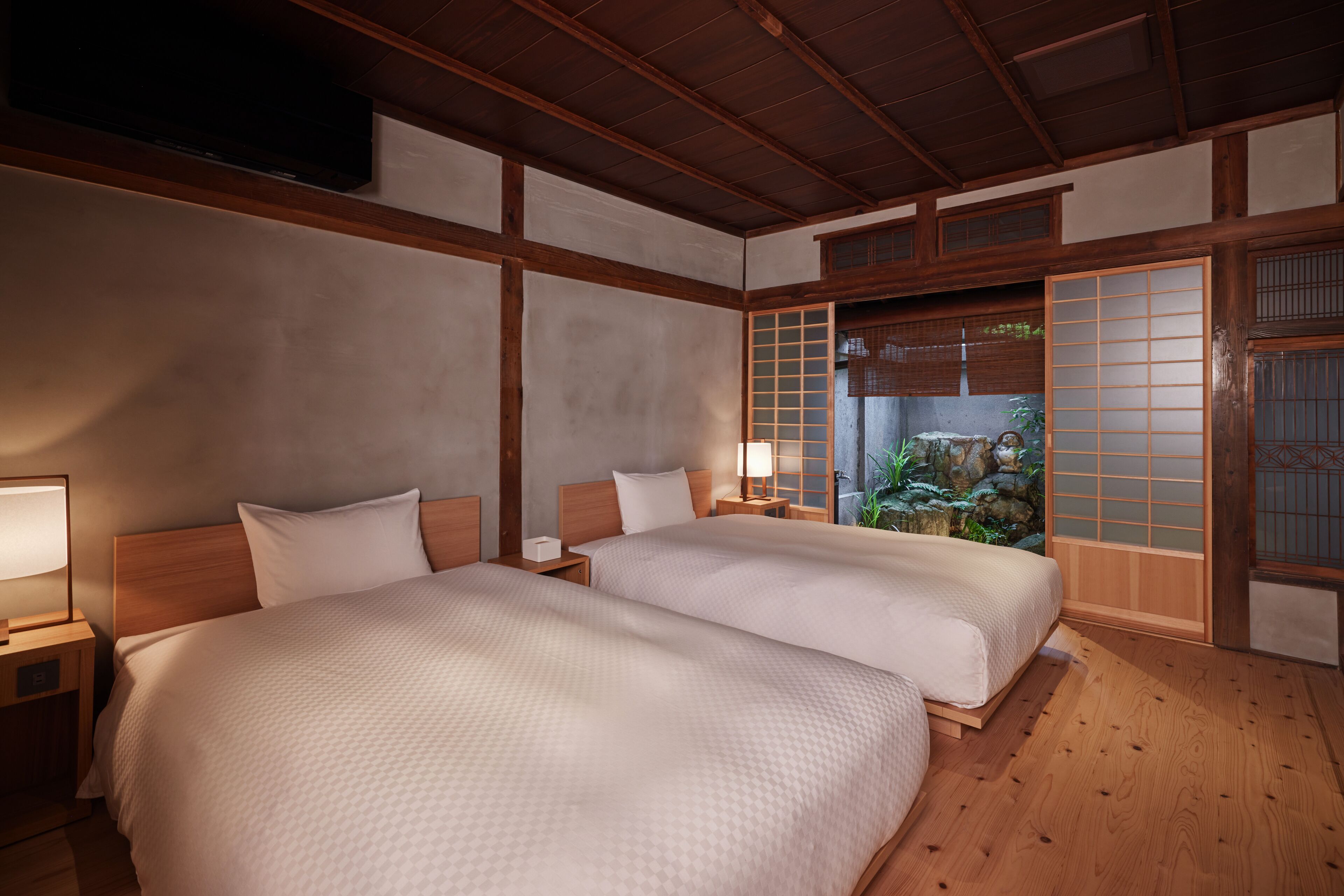 A traditional Japanese-style room with two beds, wooden flooring, and a view of a garden through a shoji screen.