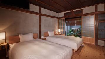 A traditional Japanese-style room with two beds, wooden flooring, and a view of a garden through a shoji screen.