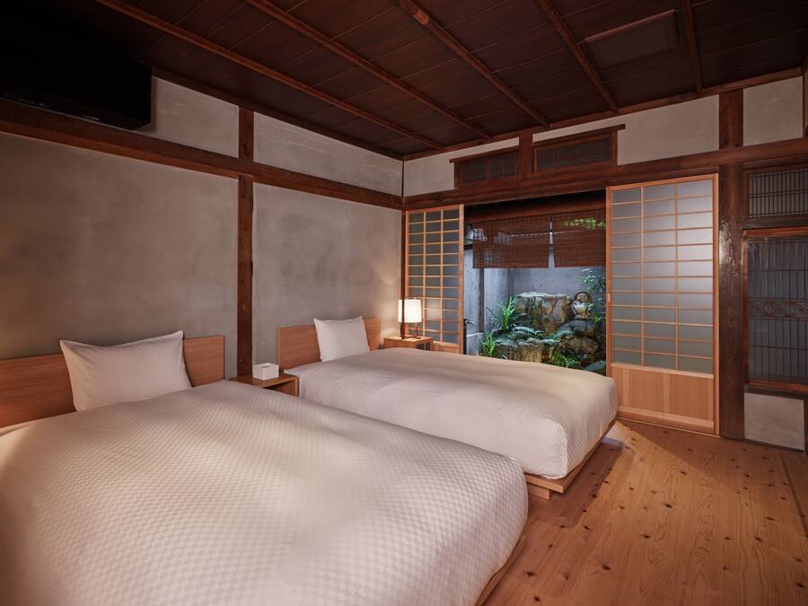 A traditional Japanese-style room with two beds, wooden flooring, and a view of a garden through a shoji screen.
