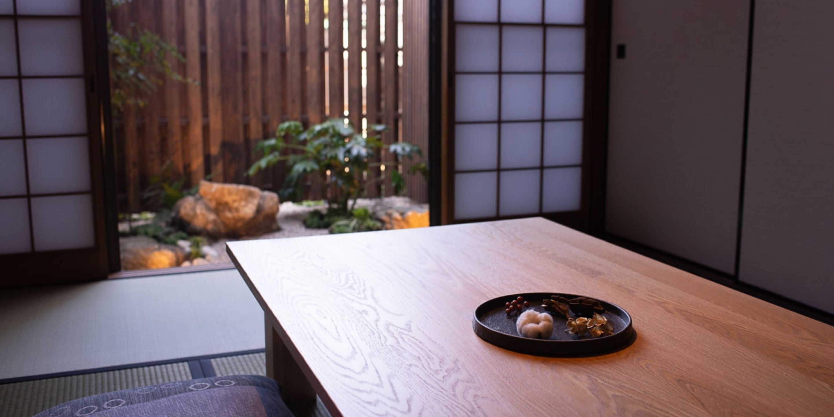 Une pièce de style japonais traditionnel, avec un sol recouvert de tatamis, une petite table en bois et une porte coulissante donnant sur un jardin agrémenté de rochers et de plantes.