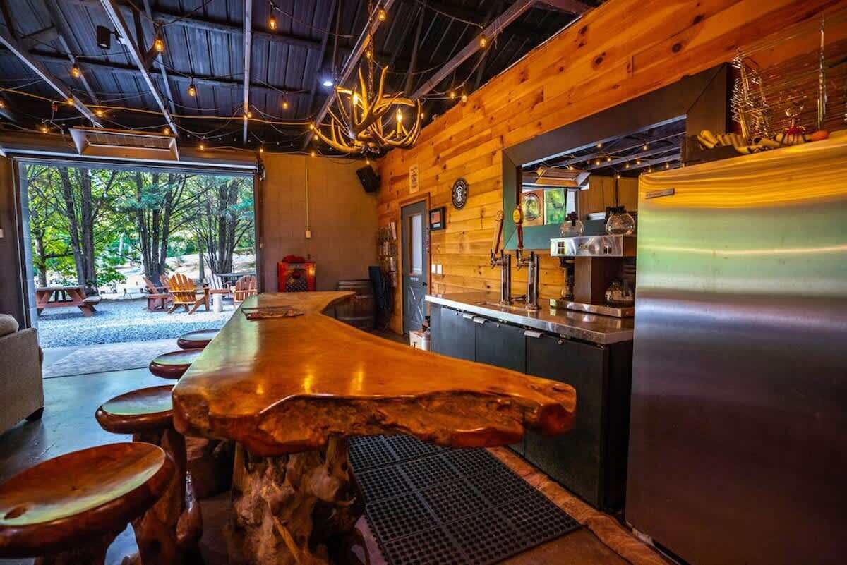 A rustic wooden interior with a bar area, a refrigerator, and a view of the outdoors.