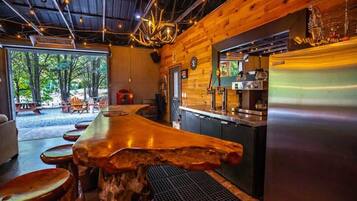 A rustic wooden interior with a bar area, a refrigerator, and a view of the outdoors.