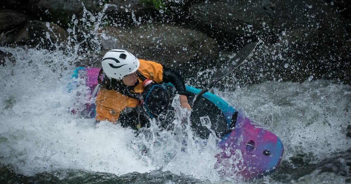 A person in a helmet and life jacket navigating a whitewater raft.