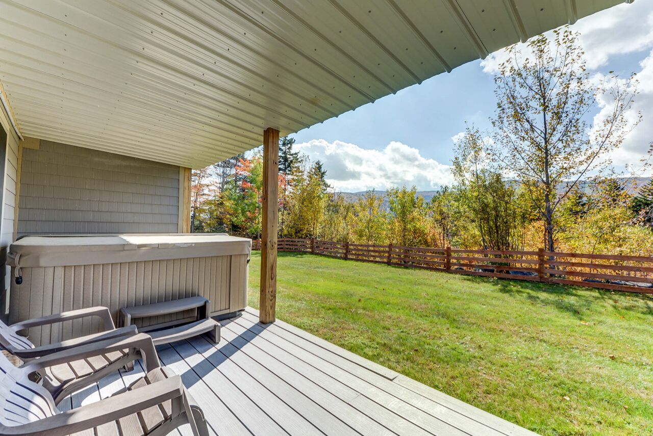 Eine überdachte Terrasse mit Whirlpool, Liegestühlen und einem Holzzaun im Hintergrund.