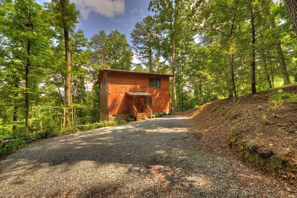 A wooden cabin with a gravel driveway, surrounded by dense forest. - Absolute Relaxation – Peaceful Cabin with Hot Tub, Firepit & Scenic Mountain Vie (Cherry Log)