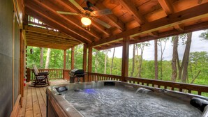 Een houten terras met een jacuzzi, een schommelstoel en een barbecue.