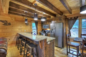 A wooden cabin kitchen with a central island, bar stools, a refrigerator, and a microwave. - Absolute Relaxation – Peaceful Cabin with Hot Tub, Firepit & Scenic Mountain Vie (Cherry Log)