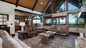A spacious living room with leather sofas, a coffee table, and a large window offering a view of the outdoors. - New Heights - Blue Ridge GA (Blue Ridge)