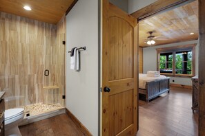 A bathroom with a wooden shower enclosure and a wooden door leading to a bedroom with a bed and a window. - New Heights - Blue Ridge GA (Blue Ridge)
