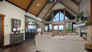 A spacious living room with a high ceiling, a fireplace, and large windows offering a view of the outdoors. - New Heights - Blue Ridge GA (Blue Ridge)