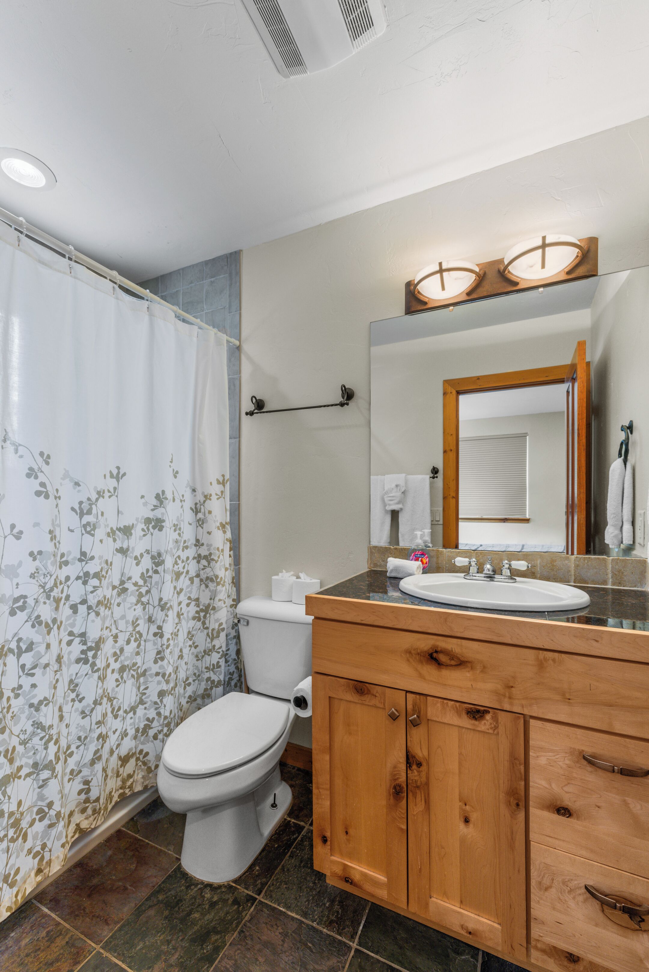 A bathroom with a shower curtain, toilet, sink, and wooden cabinets.