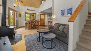 Ein geräumiger Wohnbereich mit hoher Decke, Holzbalken, Kamin, einer Couch und einem Esstisch.