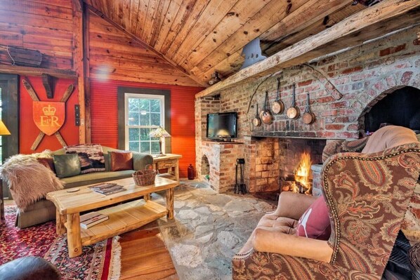 A cozy log cabin interior with a stone fireplace, wooden furniture, and a red accent wall. - Historic Cabin in Little Switzerland w/Fire Pit-Walk to village and shops! (Little Switzerland)