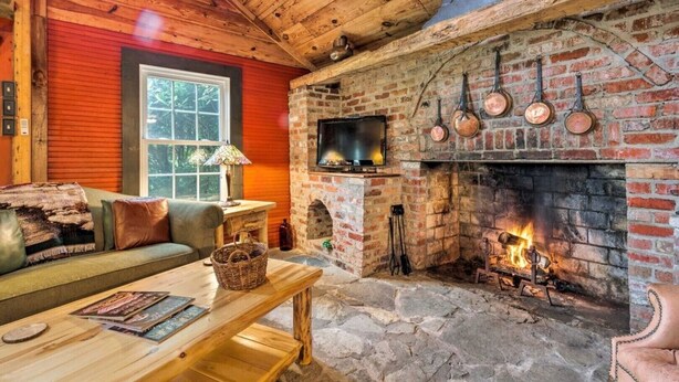 Interior acollidor d'una cabana amb una llar de pedra, una televisió penjada sobre ella i una zona de seients còmoda amb un sofà i una taula.