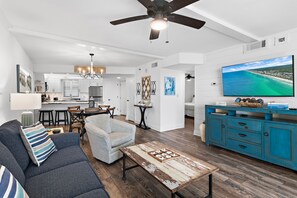 A spacious living room with a sofa, armchair, coffee table, and a television.