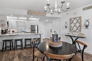 A modern kitchen with white cabinets, a stainless steel refrigerator, and a bar area with stools. - Gulf Views ~ Golf Cart ~ Community Pool ~ Balcony (Miramar Beach)