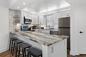 A kitchen with white cabinets, a marble countertop, and a stainless steel refrigerator.