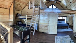 Een gezellig houten blokhut interieur met een zithoek, een bed, een tafelvoetbaltafel en een groot raam.