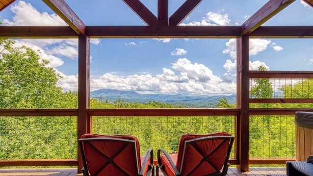 Een houten terras met twee rode stoelen gericht op een panoramisch uitzicht op de bergen.