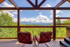 Une terrasse en bois avec deux chaises rouges donnant sur un paysage montagneux magnifique.