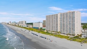 Et strandhotel med flere etager, en sandstrand og krystalklart hav.