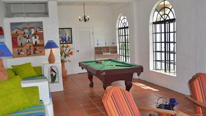 Una habitación con mesa de billar, cojines verdes, un sofá, una lámpara y un cuadro en la pared.