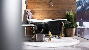 A bathroom with a freestanding bathtub, a small table with a towel, a potted plant, and a star-shaped light fixture on the wooden wall. - Apart Sailers (Sankt Anton am Arlberg)