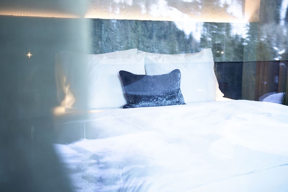 A bed with white bedding and a dark blue pillow in a room with a wooden headboard and a window with frosted glass.