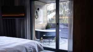 A bedroom with a bed, a sliding glass door leading to a balcony with a hot tub and a small table. - Apart Sailers (Sankt Anton am Arlberg)