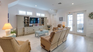 A spacious living room with a large TV, a sofa, a coffee table, and a bookshelf. - SEASONAL RENTAL - Spacious Private Pool Home - WALK TO BEACH & MERCATO (Naples)