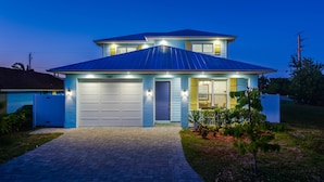 A two-story house with a garage, a well-lit entrance, and a small garden. - SEASONAL RENTAL - Spacious Private Pool Home - WALK TO BEACH & MERCATO (Naples)