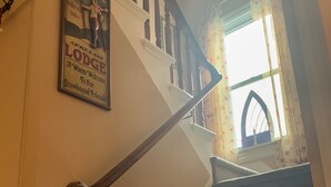 Un escalier avec une rampe en bois, une pancarte « Bienvenue » et une fenêtre ornée de rideaux à motifs floraux.