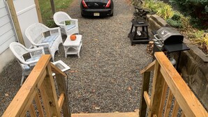 Une terrasse en gravier avec des meubles d’extérieur, un barbecue et une voiture garée à l’arrière-plan.