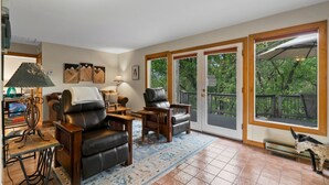 A living room with leather chairs, a coffee table, and a rug. There are two doors leading to a balcony with a view of trees. - Pickle Ball Courts, Peaceful Deck Next to Creek! (Durango)