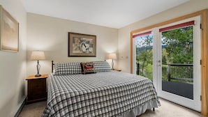 A bedroom with a large bed, two bedside tables with lamps, a framed picture on the wall, and a sliding glass door to an outdoor deck. - Pickle Ball Courts, Peaceful Deck Next to Creek! (Durango)