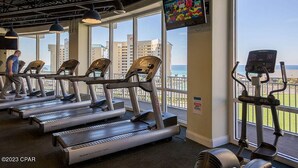 A gym with treadmills, exercise bikes, and a TV screen. -   Family Friendly 2Bedroom +Bunks, High Chair,Crib,Beach Chairs,Towels and Games (Panama City Beach)