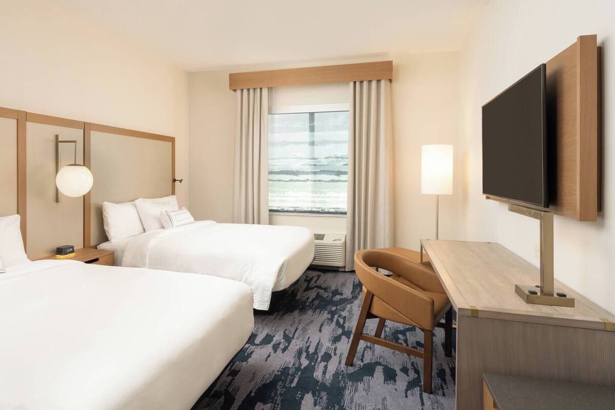 Una habitación de hotel con dos camas, un escritorio, un televisor y una ventana con cortinas.