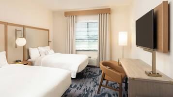 Quarto de hotel com duas camas, uma escrivaninha, televisão e janela com cortinas.