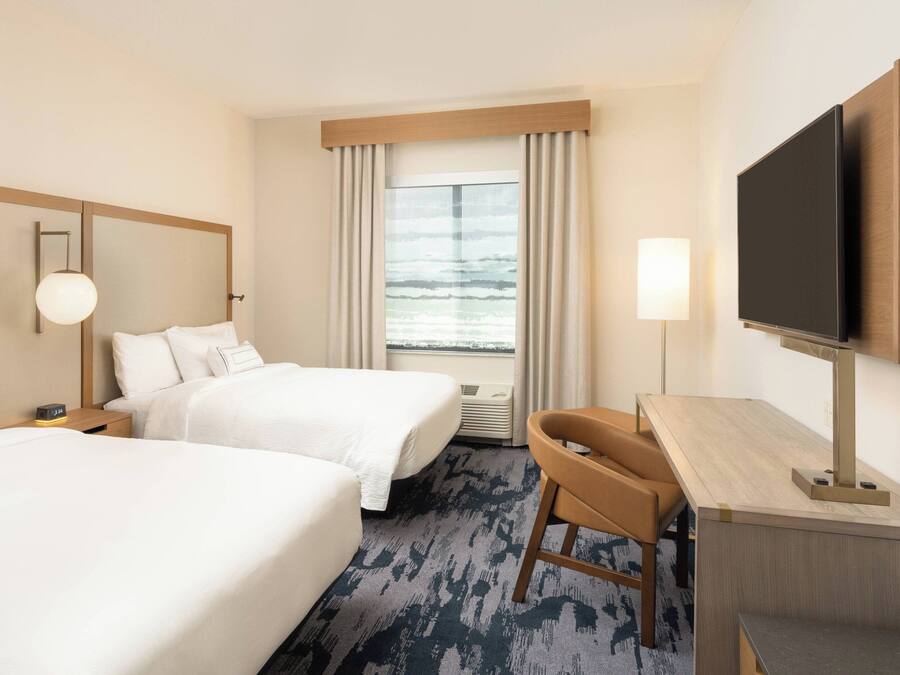 A hotel room with two beds, a desk, a TV, and a window with curtains.