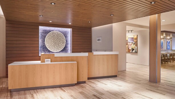 A reception area with wooden paneling, a large circular artwork on the wall, and a reception desk. - Fairfield Inn & Suites by Marriott Vero Beach (Vero Beach)