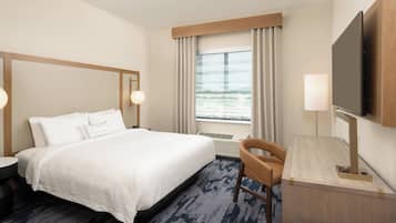 A hotel room with a large bed, a desk, a chair, a television, and a window with curtains.