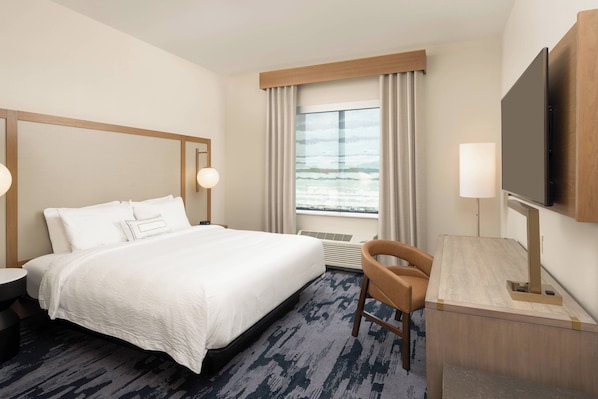 A hotel room with a large bed, a desk, a chair, a television, and a window with curtains.
