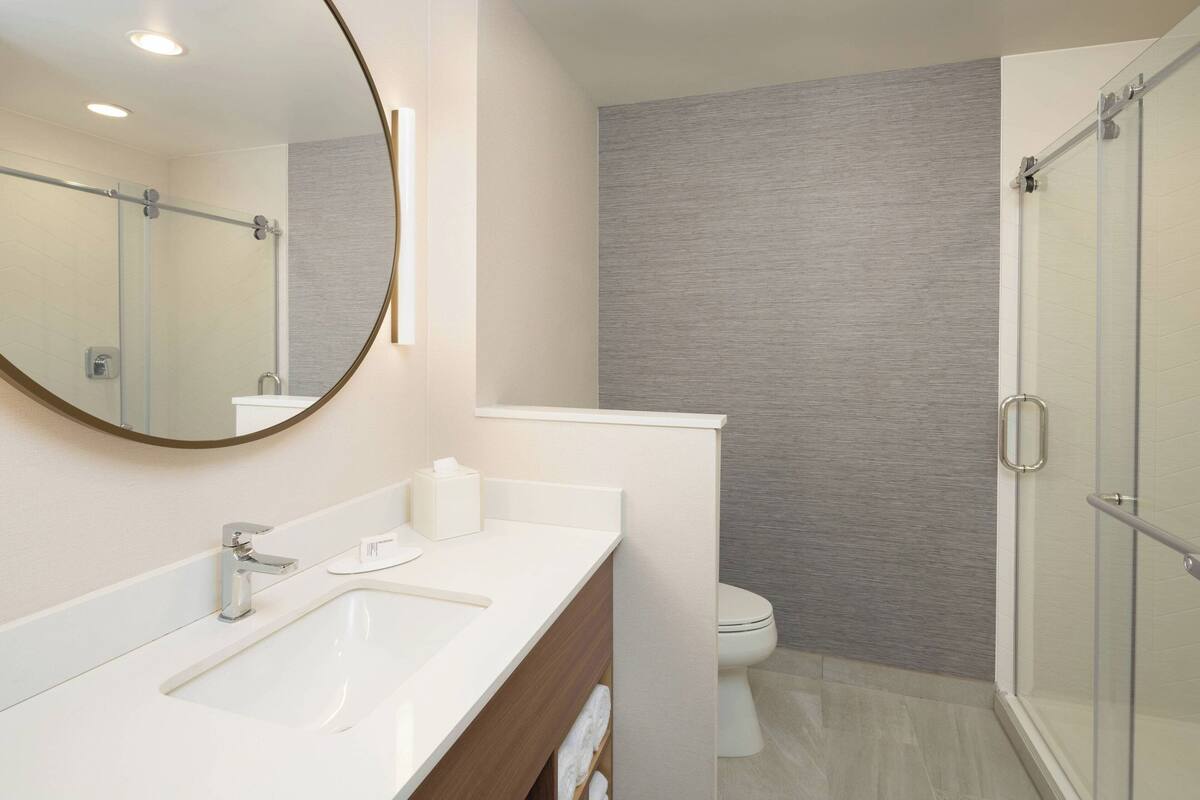Un baño moderno con un espejo grande, dos lavabos, un inodoro y una cabina de ducha de vidrio.