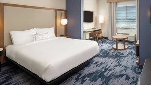 A hotel room with a large bed, a desk, a chair, a TV, and a window with a view of the ocean. - Fairfield Inn & Suites by Marriott Vero Beach (Vero Beach)