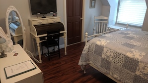 A bedroom with a bed, a desk with a chair, a television, a door, and a window. - The Prospect Room -  HSI (Idaho Falls)