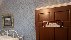 A room with a bed, a door with a sign reading "Prospect at The Historic Shelton," and a framed picture on the wall. - The Prospect Room -  HSI (Idaho Falls)