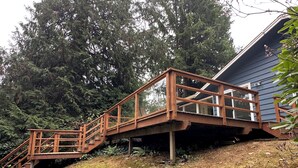 A wooden staircase leading to a deck with a view of a house and surrounding trees.