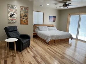A bedroom with a wooden bed, a black leather chair, a small white table, and two posters on the wall. - Newly remodeled, Steps from Downtown, Family Friendly (Cody)